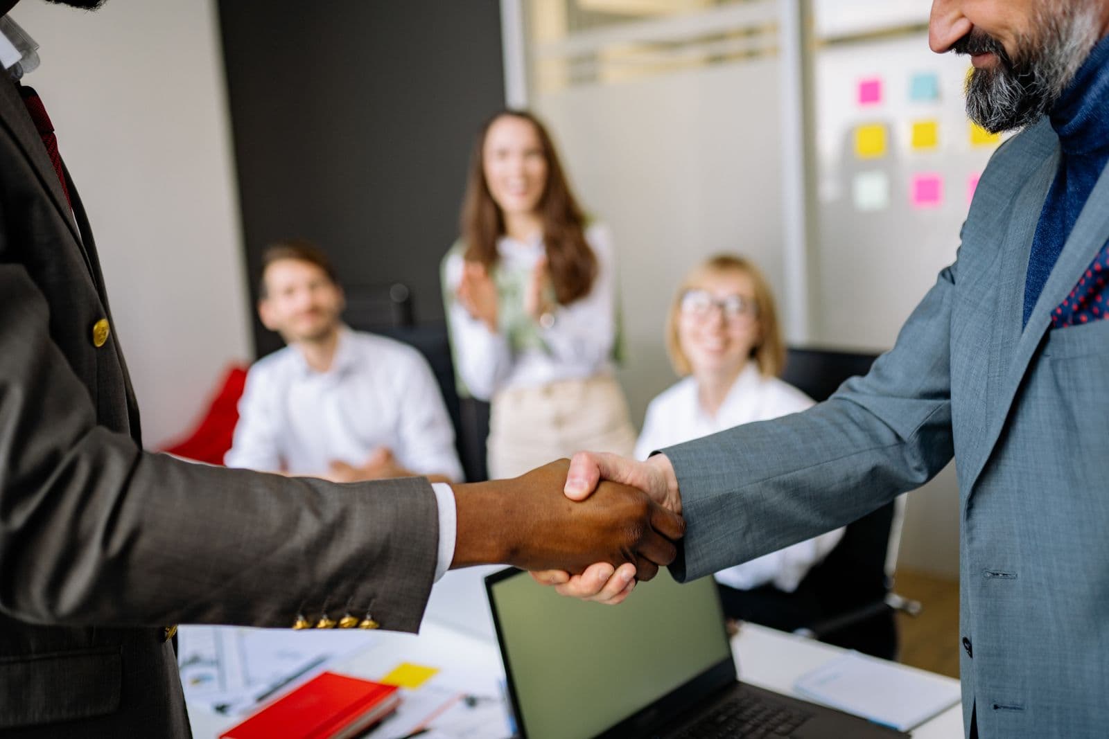 A small business owner shaking hands with an advisor while the team applauds
