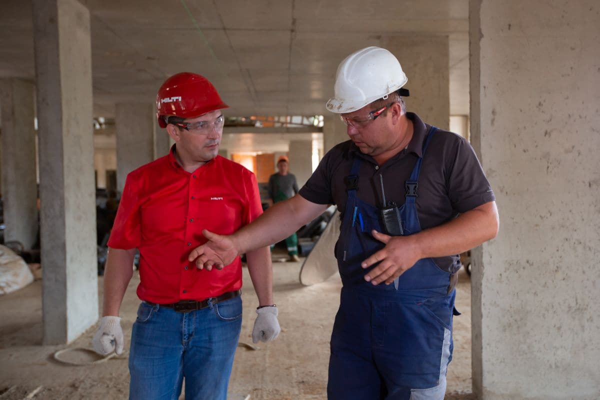 Two contract workers in hard hats talking on a job site